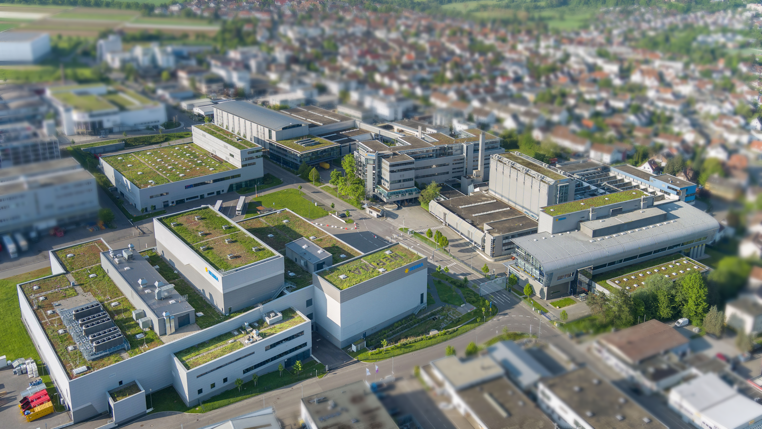 Luchtfoto van een modern bedrijventerrein met meerdere gebouwen en groene daken, omringd door een stedelijk landschap.