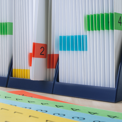 Kartonbox mit einem roten Heft auf der Oberseite, gekennzeichnet mit einem grünen "TOP"-Schild, steht auf einem Tisch.