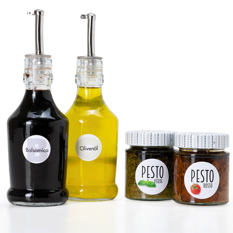 Twee flessen balsamico en olijfolie, evenals twee glazen pesto in verschillende smaken op een witte achtergrond.