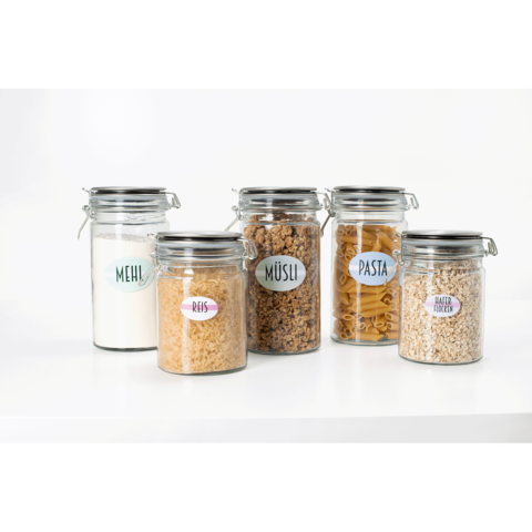 Fünf Gläser mit Lebensmitteln: Mehl, Reis, Müsli, Pasta und Haferflocken, jeweils mit beschrifteten Etiketten.