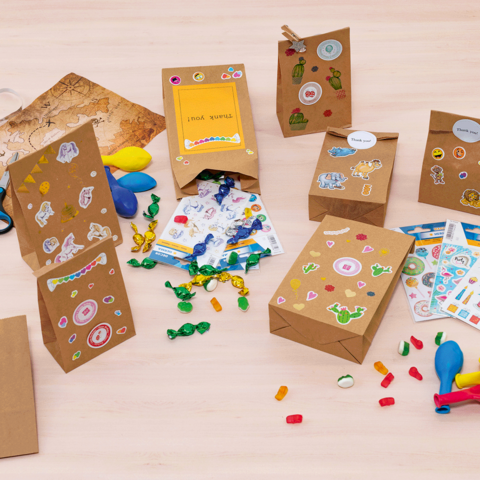 Kleurige cadeautasjes en knutselmaterialen op een tafel, waaronder stickers, ballonnen, scharen en snoepjes.