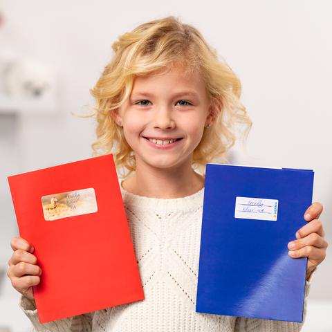 Een glimlachend kind houdt een rood en een blauw schrift in de handen, beide met stickers.