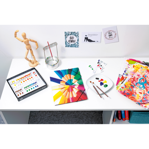 Ein Tisch mit Malutensilien, darunter Wasserfarben, Pinsel, Farbpaletten und ein Holzmodell. An der Wand hängen inspirierende Zitate.