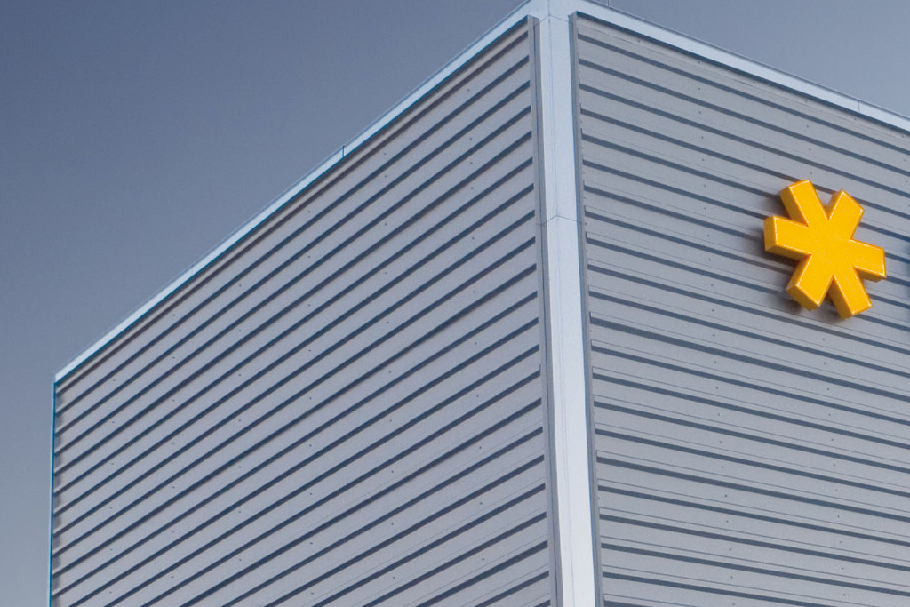 Gevel van een modern gebouw met het logo van HERMA in blauwe letters en een geel symbool.