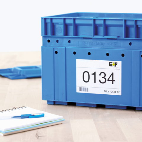 Blaue Kunststoffbox mit einer Etikette, die die Nummer 0134 und die Maße 10 x 4220.17 zeigt, neben einem Notizblock und einem Stift.