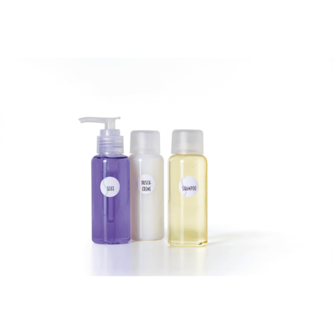 Drei Flaschen mit Pflegeprodukten: eine lila Flasche mit Pumpkopf, eine weiße Flasche und eine gelbe Flasche, beschriftet mit "Shampoo".