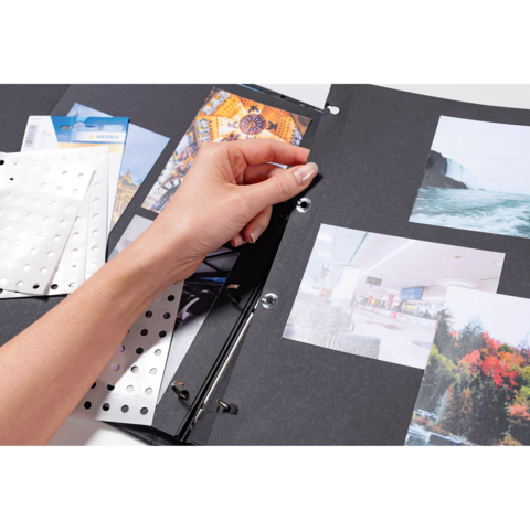 Eine Hand blättert durch einen Fotoalbum mit verschiedenen Bildern und Aufklebern auf schwarzem Hintergrund.