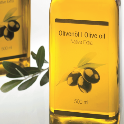 Flasche mit Olivenöl, 500 ml, mit Etikett "Olivenöl | Olive oil" und "Native Extra", umgeben von Olivenzweigen.