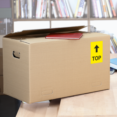 Ein Karton mit dem Aufkleber "FRAGILE", daneben ein graues Kuvert mit dem Aufkleber "URGENT!" und eine Schere.