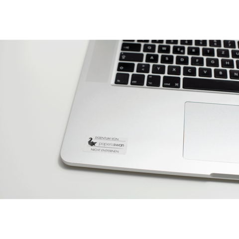 Ein Laptop mit einer Tastatur und einem Aufkleber, der "EIGENTUM VON paperswan" und "NICHT ENTFERNEN" zeigt.
