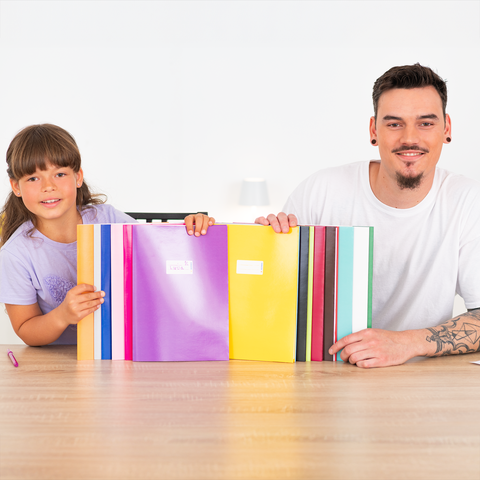 Ein Mann und ein Mädchen sitzen an einem Tisch und halten bunte Ordner. Der Mann trägt ein weißes T-Shirt und hat Tattoos.