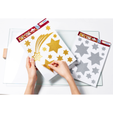 Hände halten glitzernde Sterne und eine Sternschnuppe auf zwei Bogen. Ein Bogen ist goldfarben, der andere silberfarben.