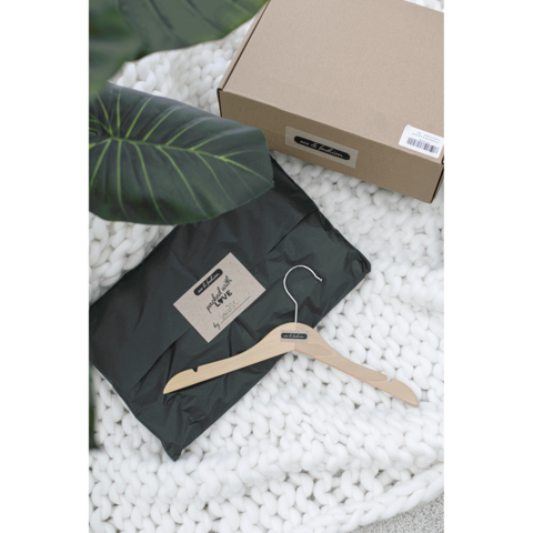 Ein schwarzes Paket mit einem Aufkleber, ein Holzkleiderbügel und eine weiße, gestrickte Decke im Hintergrund.