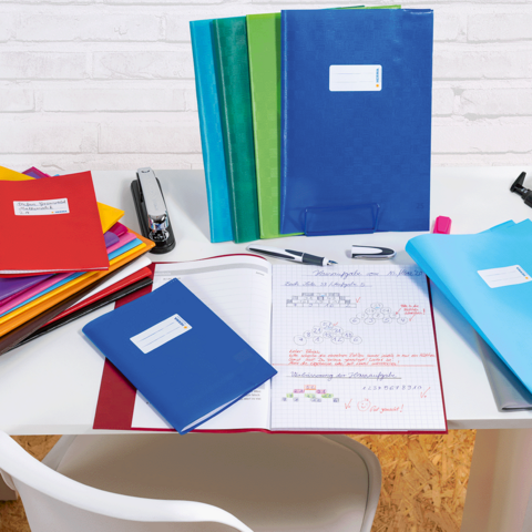 Verschillende gekleurde mappen en notitieboeken op een tafel, daarnaast een perforator en schrijfgerei.