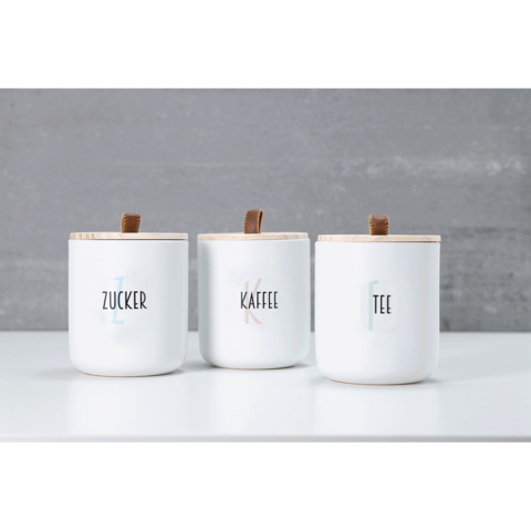 Drei weiße Behälter mit Holzdeckeln, beschriftet mit "Zucker", "Kaffee" und "Tee".