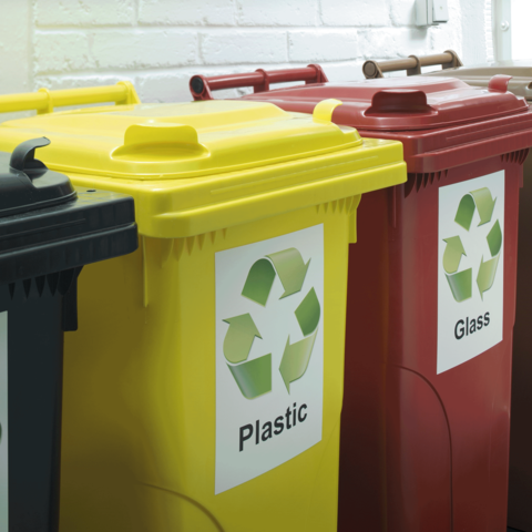Drei Abfallbehälter in verschiedenen Farben mit Recycling-Symbolen: Gelb für Plastik, Rot für Glas und Schwarz für Restmüll.