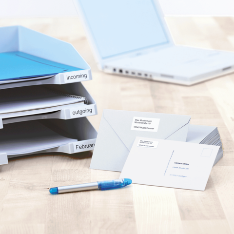 Ordner mit Beschriftungen für eingehende und ausgehende Dokumente, dazu Umschläge und ein blauer Stift auf einem Tisch.