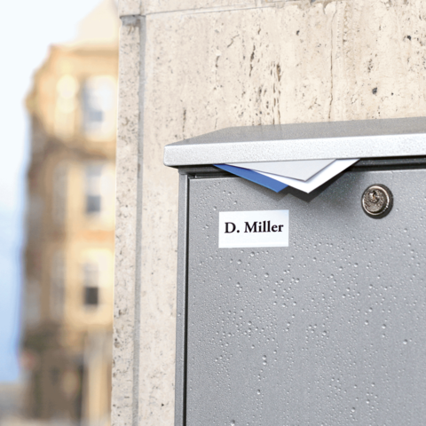 Graue Briefkasten mit dem Namen "D. Miller" auf einem Gehweg, leicht feucht von Regen.