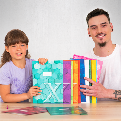 Ein Junge und ein Mann lächeln, während sie bunte, geometrische Ordner auf einem Tisch präsentieren.