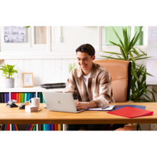 Ein junger Mann sitzt an einem Schreibtisch mit einem Laptop, umgeben von Büromaterialien und Pflanzen, während er arbeitet.