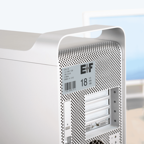 Silberner Computer mit perforierter Rückseite, ausgestattet mit mehreren Anschlüssen und einem Etikett mit technischen Spezifikationen.