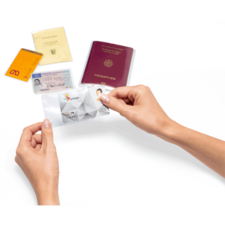 Eine Hand hält eine transparente Hülle mit einer ID-Karte, während im Hintergrund ein Reisepass und mehrere andere Ausweisdokumente liegen.