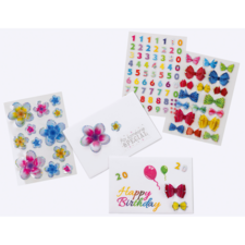 Bunte Aufkleber mit Blumen, Zahlen und Schleifen, sowie eine Geburtstagskarte mit der Aufschrift "Happy Birthday" und Luftballons.