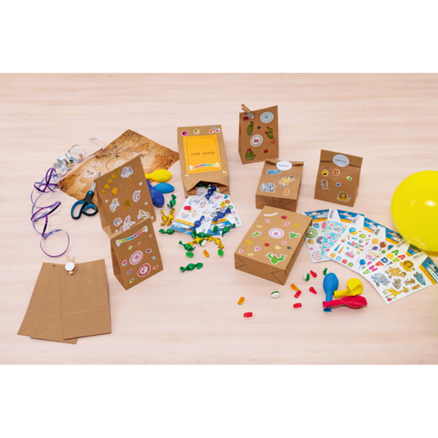 Bunte Geschenktüten und -boxen aus Kraftpapier, dekoriert mit Aufklebern, umgeben von Bastelmaterialien wie Scheren, Luftballons und Süßigkeiten.