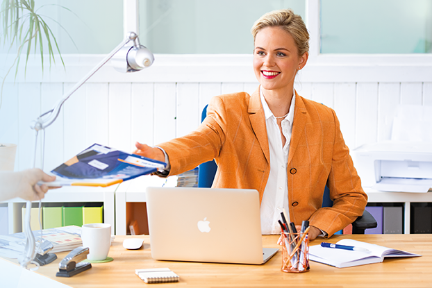 Twee personen aan een tafel die etiketten presenteren. Links een man met etikettenvellen, rechts een vrouw met een laptop en etiketten.